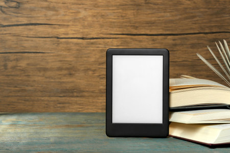 Portable e-book reader and open hardcover books on wooden rustic table, space for text