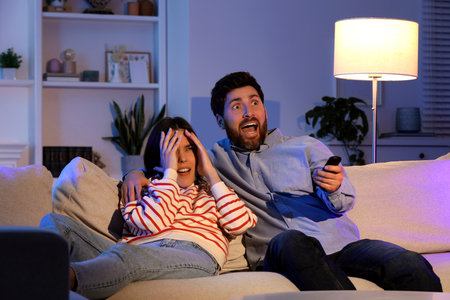 Frightened couple watching TV on sofa at homeの写真素材