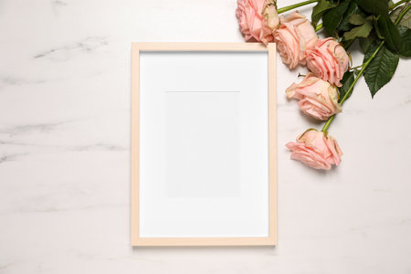 Empty photo frame and beautiful flowers on white marble background, flat lay. Space for designの写真素材