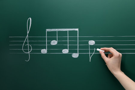 Woman writing musical notes with chalk on blackboard, closeup