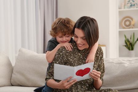 Little son congratulating his mom with Mother`s day at home. Woman holding handmade greeting cardの写真素材