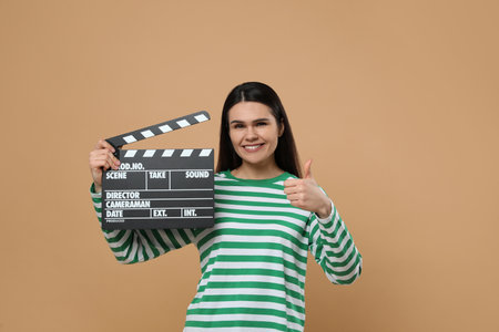 Happy actress with clapperboard showing thumbs up on beige background. Film industryの写真素材