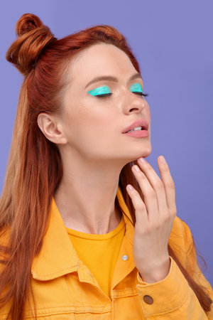 Beautiful woman with bright makeup and closed eyes posing on violet backgroundの写真素材