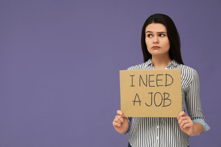 Unemployment problem. Unhappy woman holding sign with phrase I Need A Job on violet background. Space for textの写真素材