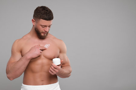 Handsome man applying body cream onto his chest on light gray background, space for textの写真素材