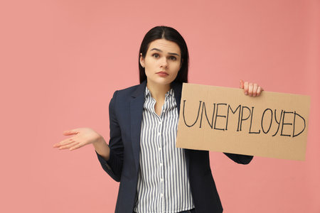Unhappy woman holding sign with word Unemployed on pink backgroundの写真素材