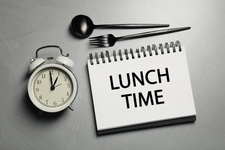 Business lunch. Notebook with phrase Lunch Time, cutlery and alarm clock on light gray table, flat layの写真素材