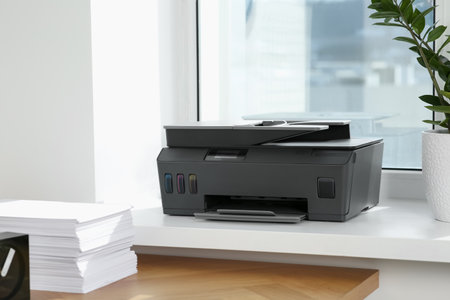 Stack of paper on wooden table near window sill with modern printer in officeの写真素材
