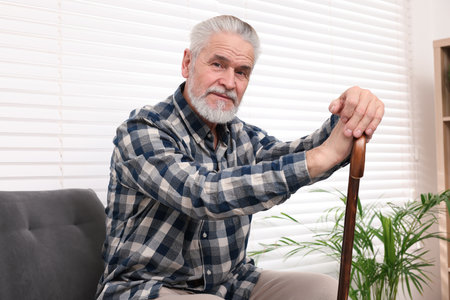 Senior man with walking cane sitting on armchair at home