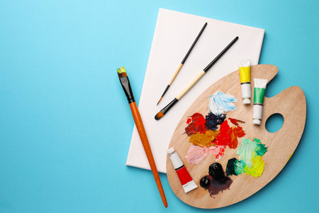 Blank canvas, tubes of oil paints, brushes and palette on light blue background, top view. Space for textの写真素材