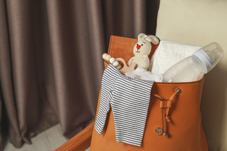 Mother's bag with baby's stuff on armchair indoors. Space for text