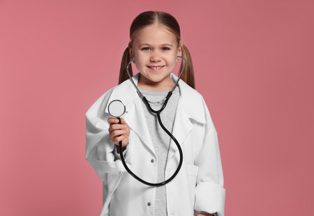 Little girl in medical uniform with stethoscope on pink backgroundの写真素材