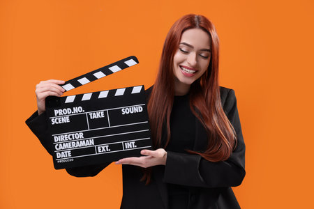 Happy actress with clapperboard on orange background. Film industryの写真素材