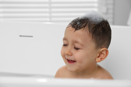 Cute little boy washing hair with shampoo in bathroom. Space for text