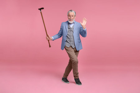 Senior man with walking cane on pink backgroundの写真素材