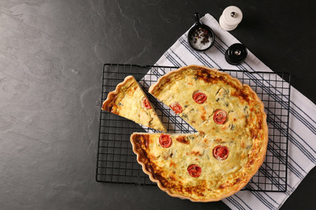 Delicious homemade cheese quiche and spices on black table, flat lay