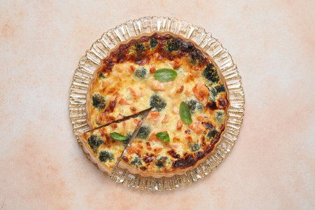 Delicious homemade quiche with salmon and broccoli on beige table, top viewの写真素材