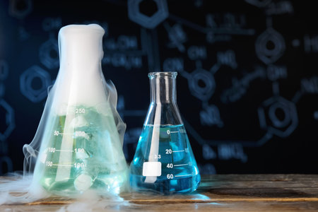 Laboratory glassware with colorful liquids and steam on wooden table against black background, space...