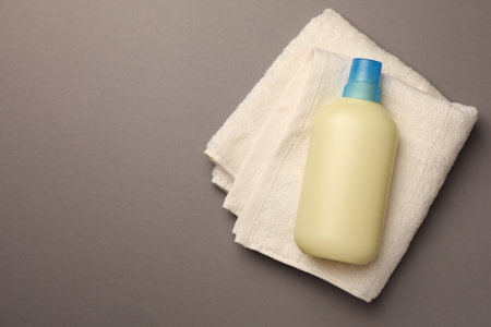 Bottle of fabric softener and terry towel on gray background, top view. Space for textの写真素材
