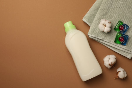 Flat lay composition with bottle of fabric softener and laundry detergent pods on brown background, space for textの写真素材