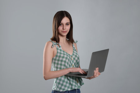 Cute teenage girl with laptop on light grey backgroundの写真素材
