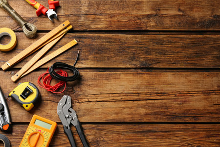 Wires and electrician's tools on wooden table, flat lay. Space for text