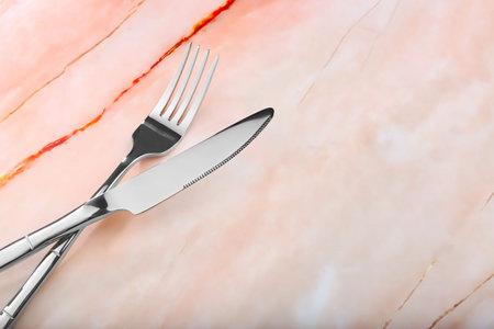 Shiny fork and knife on pink marble table, closeup. Space for text
