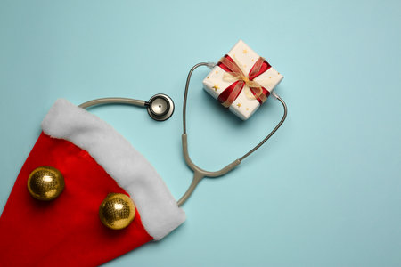 Greeting card for doctor with stethoscope, gift box, Santa hat and Christmas decor on light blue background, flat layの写真素材