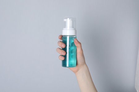 Woman holding bottle of face cleansing product on white background, closeup