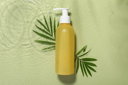 Bottle of facial cleanser and leaves in water against olive background, flat layの写真素材