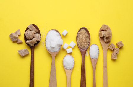 Spoons with different types of sugar on yellow background, flat layの写真素材