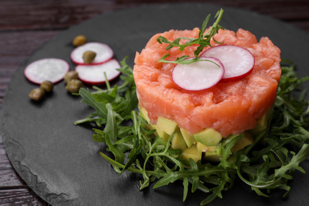 Tasty salmon tartare with radish, avocado and arugula on wooden table, closeupの写真素材