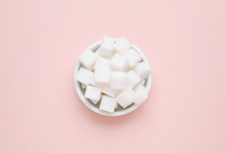 Refined white sugar cubes in bowl on pink background, top viewの写真素材
