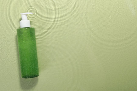 Bottle of facial cleanser in water against olive background, top view. Space for textの写真素材