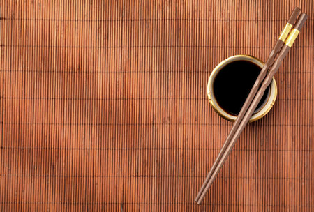 Bowl of soy sauce and chopsticks on bamboo mat, flat lay. Space for textの写真素材