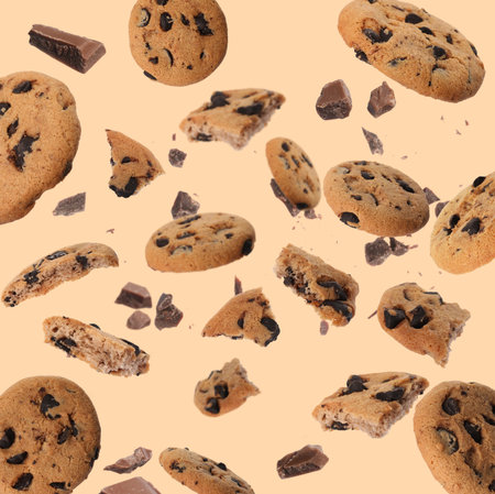 Delicious chocolate chip cookies and pieces of chocolate falling on beige backgroundの写真素材