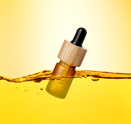 Bottle of cosmetic product floating in essential oil against gold gradient backgroundの写真素材