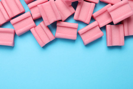 Tasty pink chewing gums on light blue background, flat lay. Space for textの写真素材