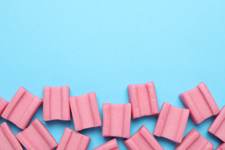 Tasty pink chewing gums on light blue background, flat lay. Space for textの写真素材