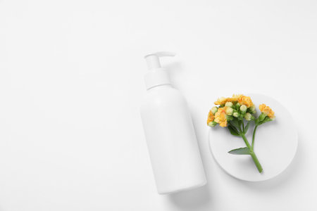 Bottle of cosmetic product, flowers and podium on white background, flat lay. Space for textの写真素材