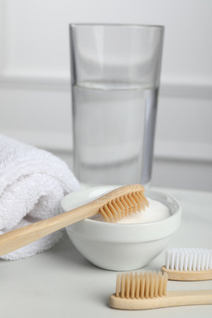 Bamboo toothbrushes, bowl of baking soda, towel and glass of water on white tableの写真素材