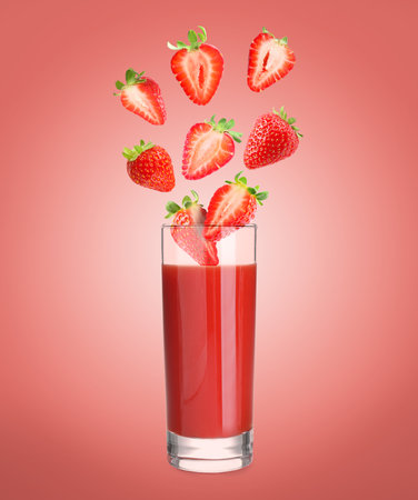 Freshly made strawberry juice on pale red background. Cut and whole berries falling into glassの写真素材