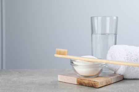 Bamboo toothbrush, bowl of baking soda, towel and glass of water on gray table, space for textの写真素材