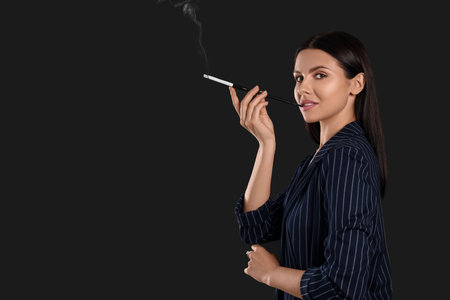 Woman using long cigarette holder for smoking on black background, space for textの写真素材