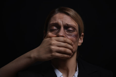 Kidnapper covering mouth of woman taken hostage on dark background