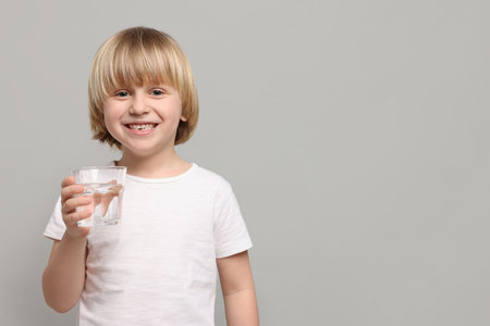 Happy little boy holding glass of fresh water on light grey background. Space for textの写真素材