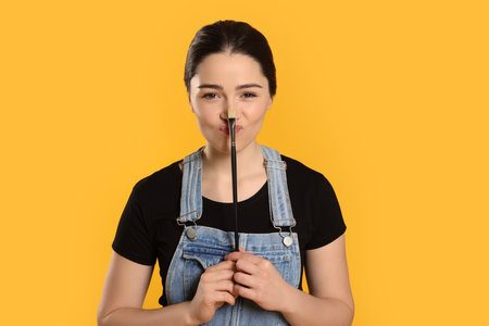 Woman with paintbrush on yellow background. Young artistの写真素材