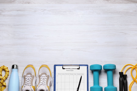 Personal training. Clipboard with workout plan, sneakers and sports equipment on white wooden table,...