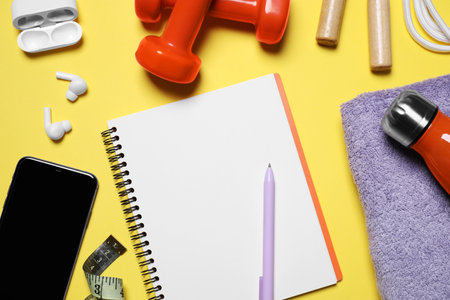 Notebook, smartphone and sports equipment on yellow background, flat lay. Personal trainingの写真素材