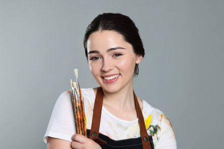 Woman with paintbrushes on grey background. Young artistの写真素材